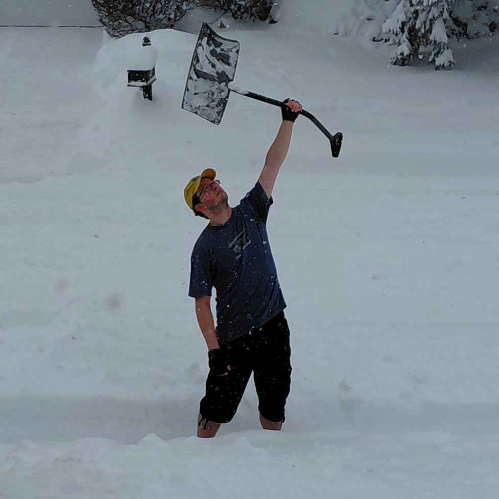 Man with snow shovel in knee-deep snow.